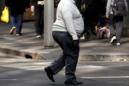 A man crosses a main road as pedestrians carrying food walk along the footpath in central Sydney, Australia